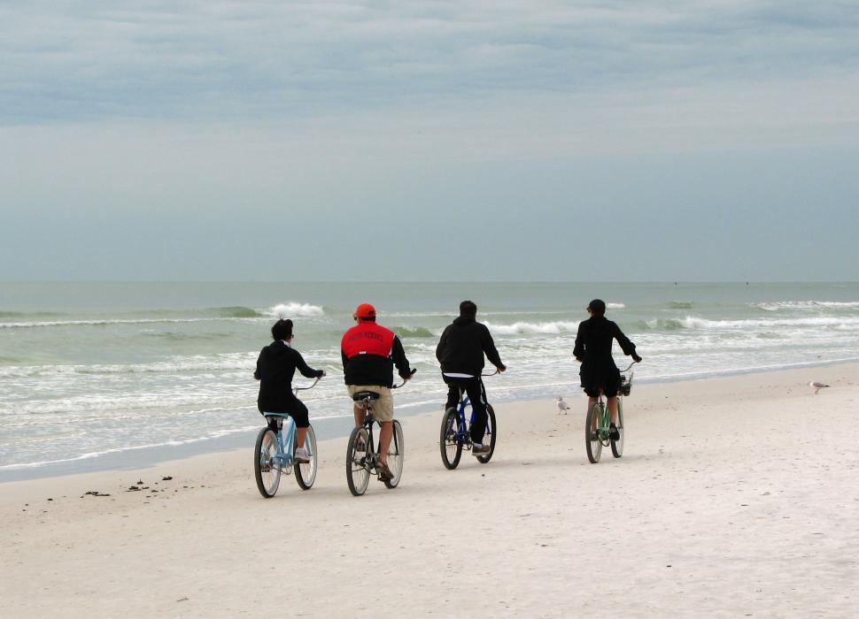 Free Image of People riding bikes on the beach by the ocean 