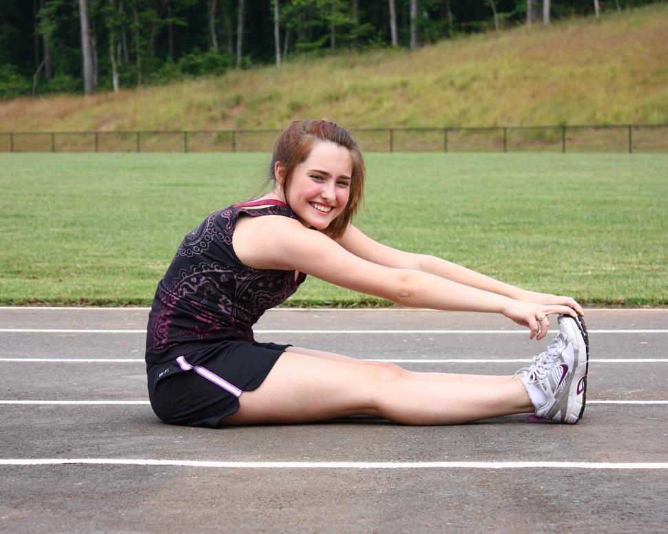 Free Image of A cute young girl doing stretches on a track field 
