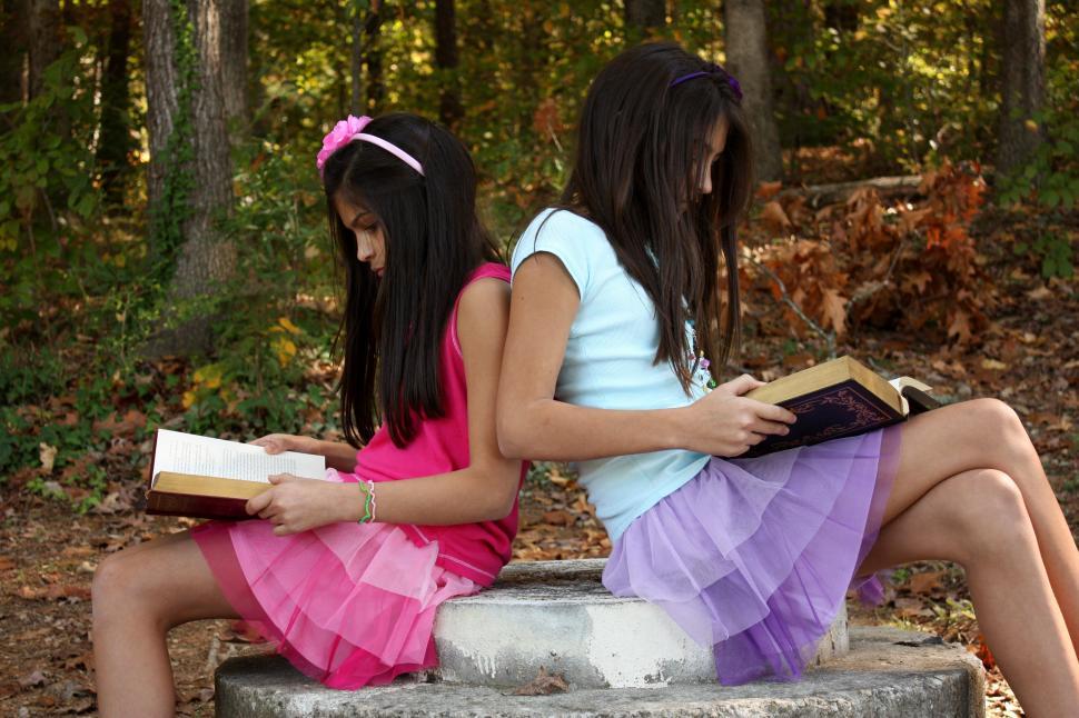 Free Image of Two cute young girls reading books outdoors 