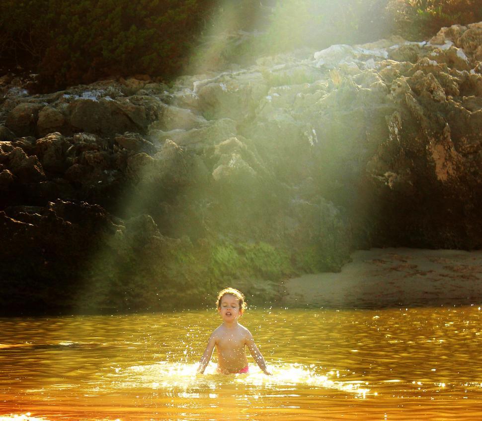 Free Image of Child hit by sun rays bathing in golden water 