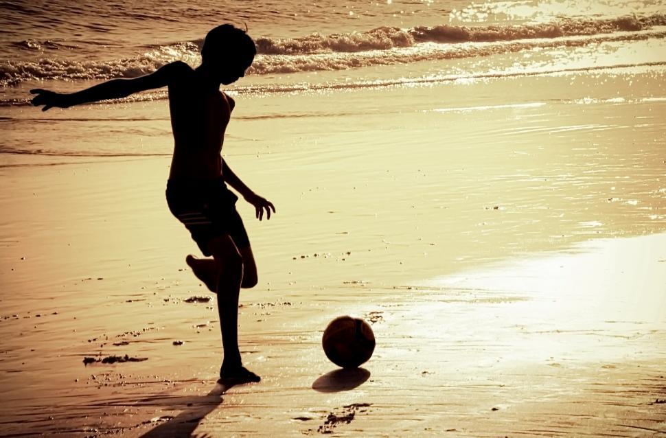 Free Image of Silhouette of boy on the beach playing football 