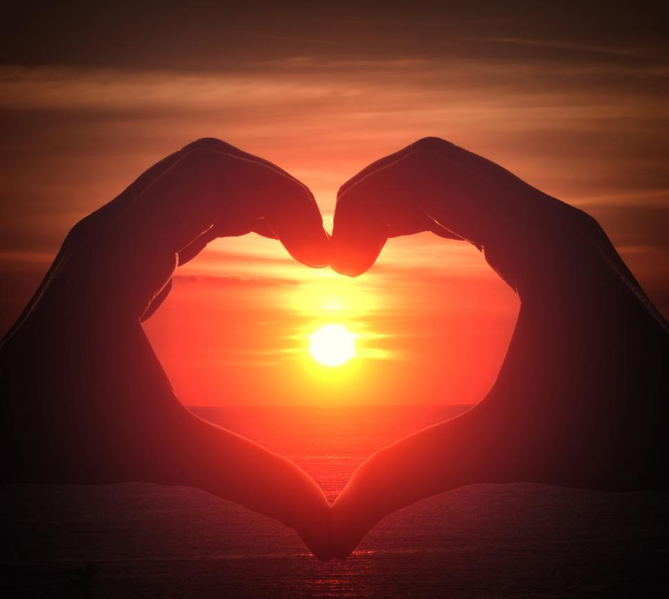 Free Image of Hand silhouette in heart shape with sunset in the middle and oce 