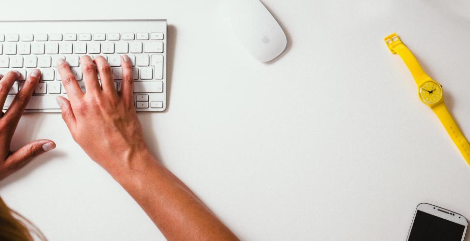 Free Image of Person Typing on Computer Keyboard Next to Cell Phone 