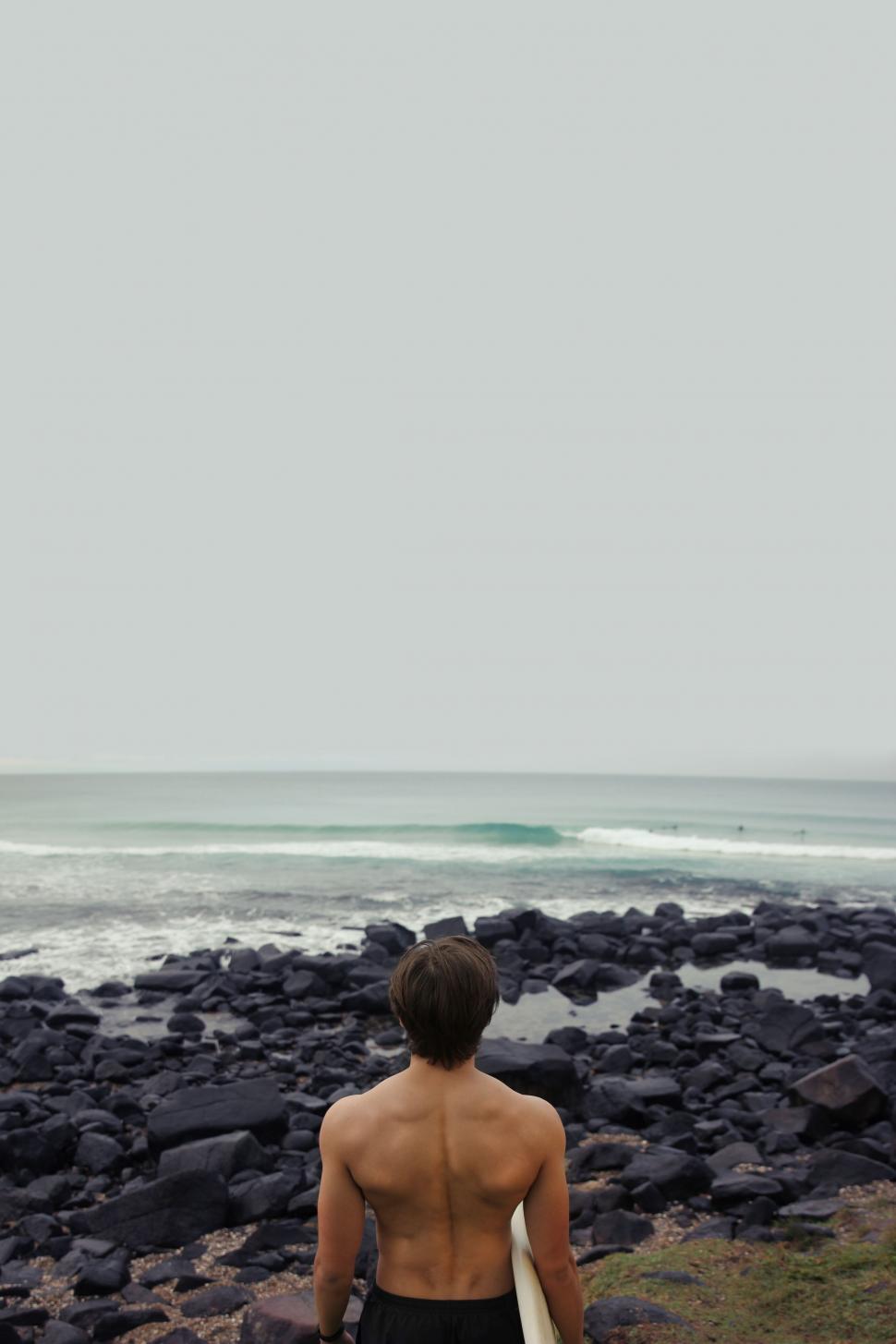 Free Image of Man Walking on Rocky Beach With Surfboard 