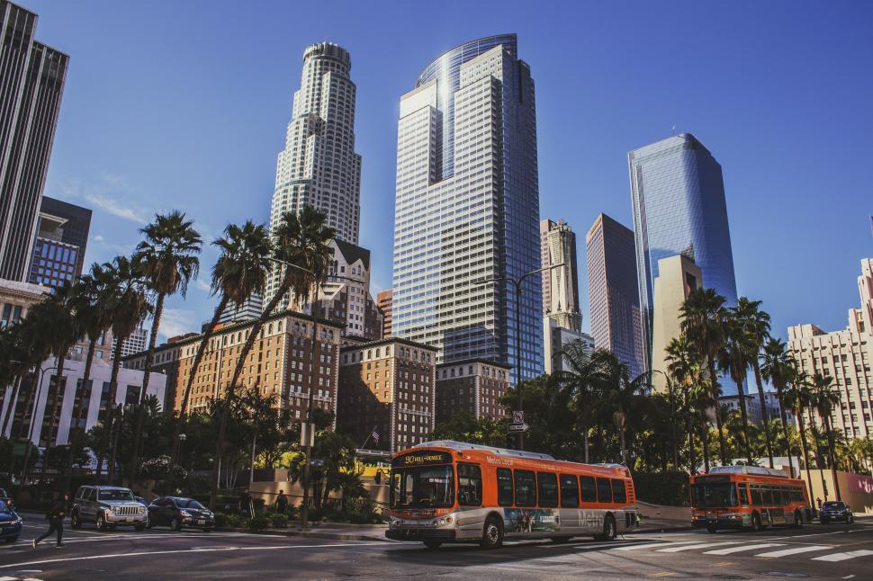 Free Image of Red Bus Driving Down Street Next to Tall Buildings 