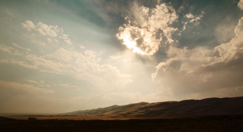 Free Image of Sun Shining Through Clouds Over Hills 