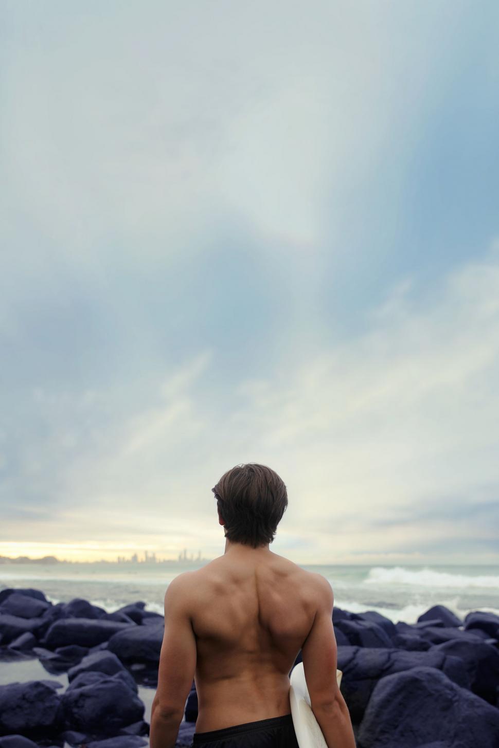 Free Image of Man Holding Surfboard on Rocky Beach 
