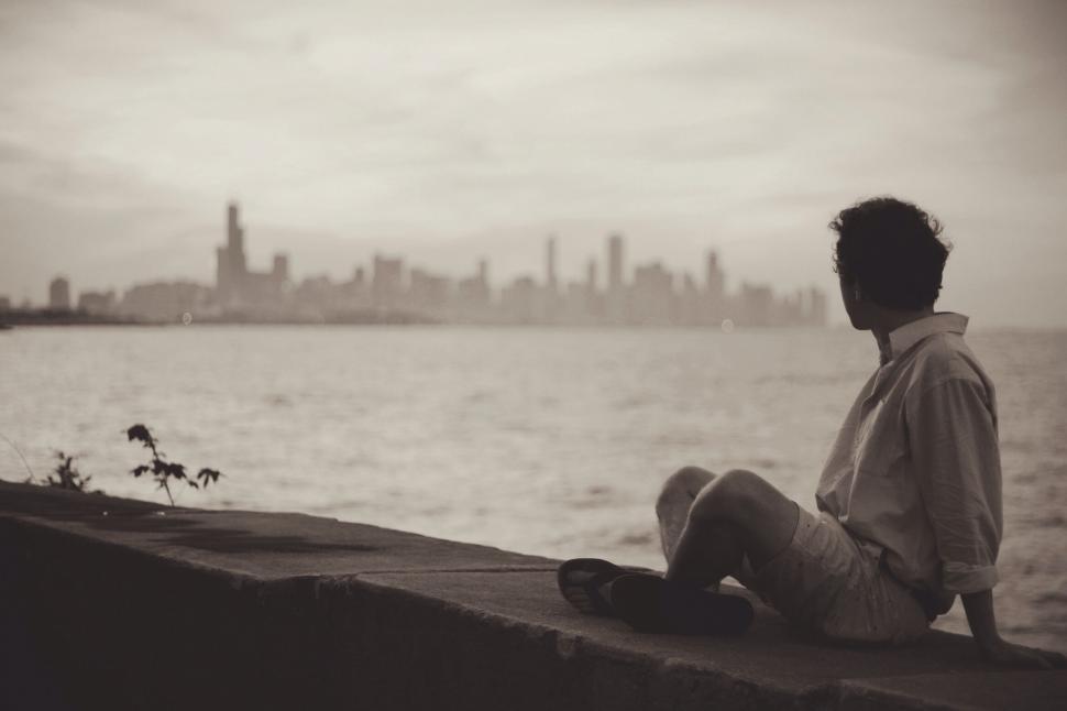 Free Image of Man Sitting on Ledge Overlooking Water 