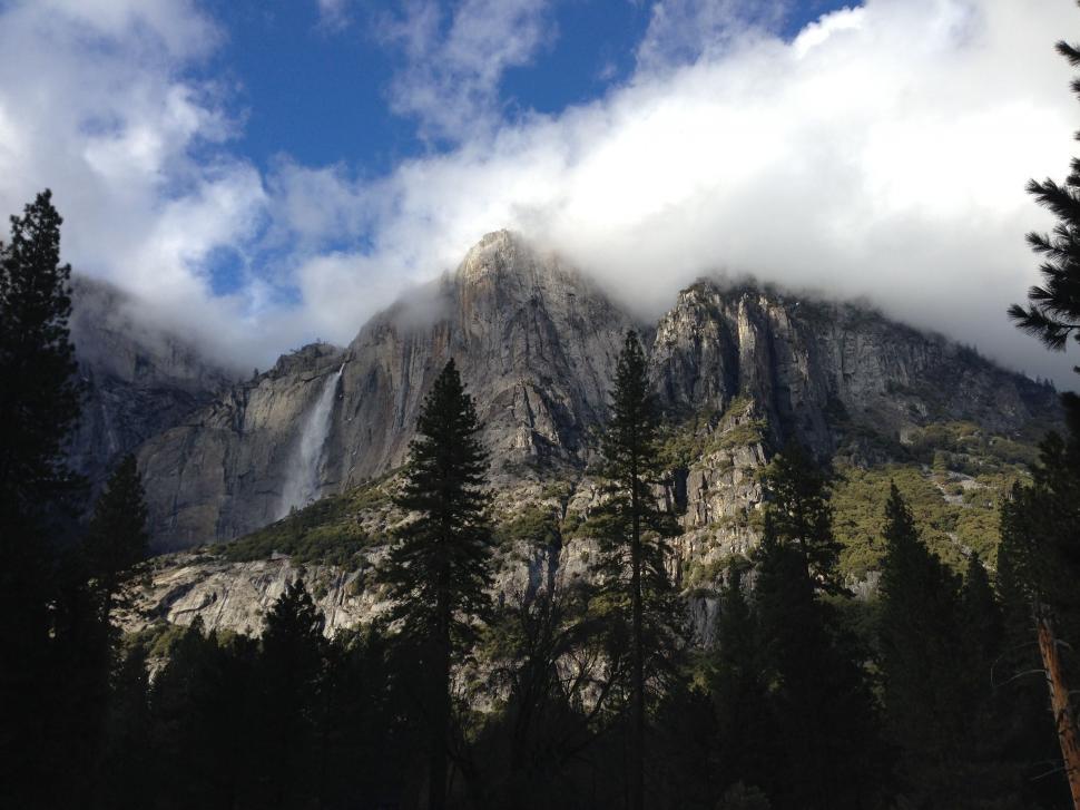 Free Image of Mountain Covered in Clouds and Trees Under Blue Sky 