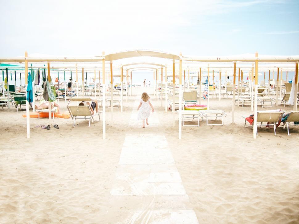 Free Image of Woman Walking Along Sandy Beach Filled With Chairs 