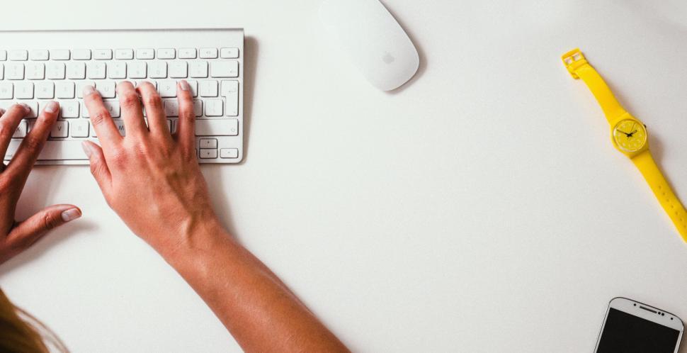 Free Image of Person Typing on Keyboard Next to Cell Phone 