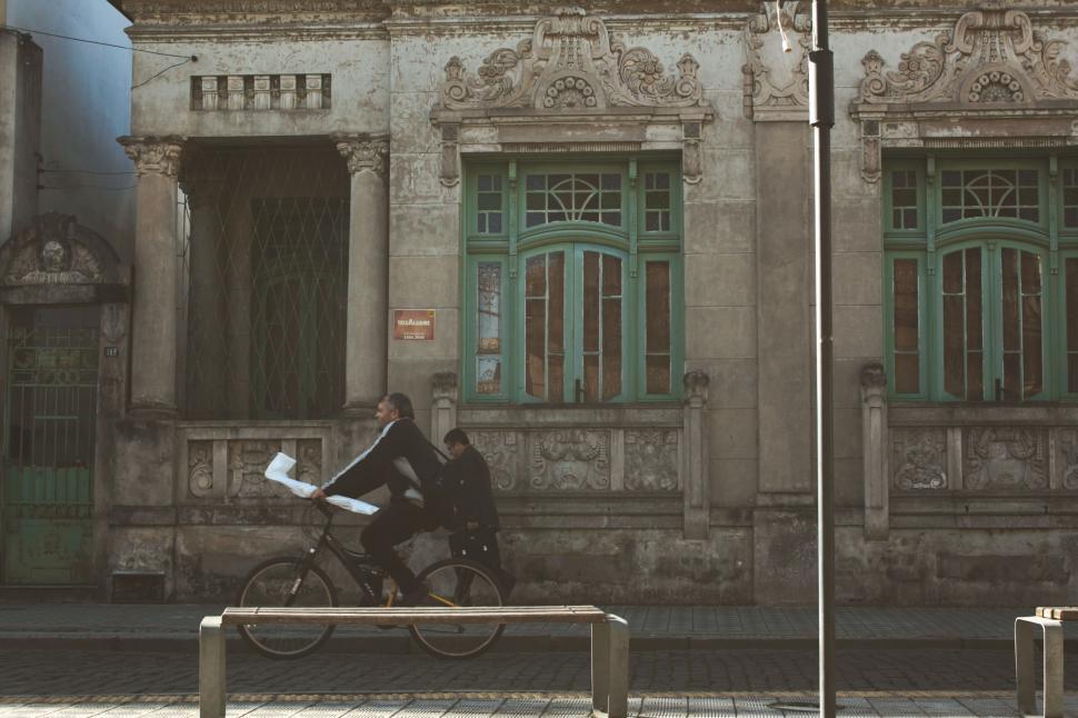 Free Image of Man Riding Bike Past Tall Building 