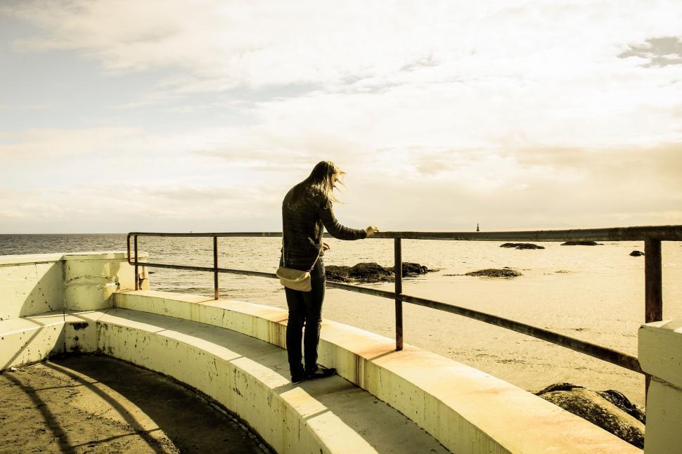 Free Image of Woman Standing on Railing Near Ocean 