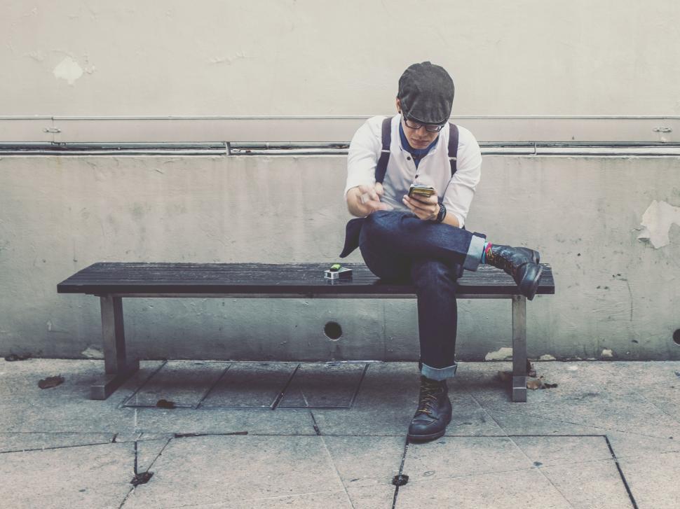 Free Image of Man Sitting on Bench Looking at Cell Phone 