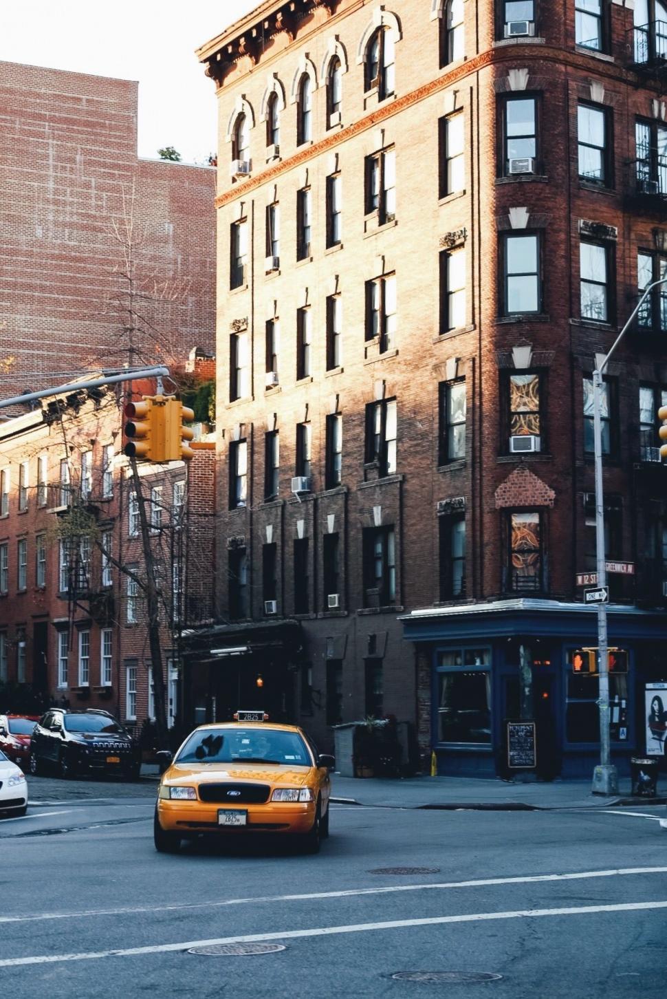 Free Image of Yellow Taxi Cab Driving Down Street Next to Tall Buildings 