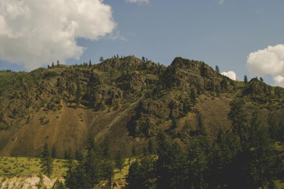 Free Image of Mountain Covered in Trees Under a Cloudy Blue Sky 