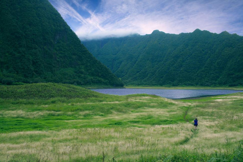 Free Image of Man Walking Through Lush Green Field Next to Lake 