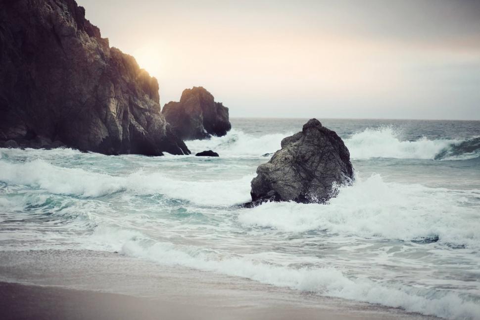 Free Image of Large Rock Protruding From Ocean by Beach 