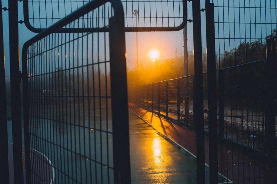 Free Image of Sun Setting Behind Fence on Rainy Day 
