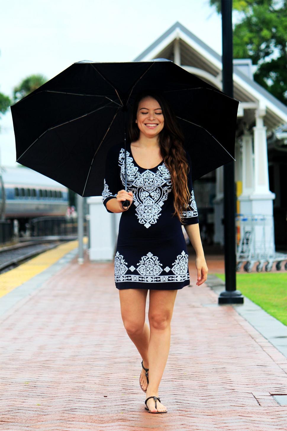 Free Image of Woman Walking Down Sidewalk Holding Umbrella 