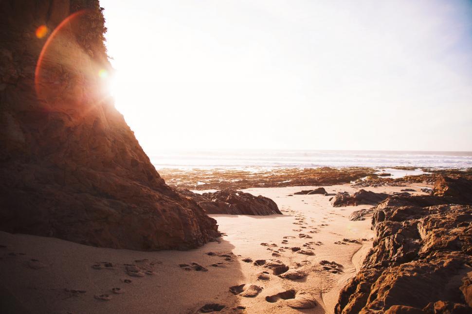 Free Image of Sun Shining Through Rocks on Beach 