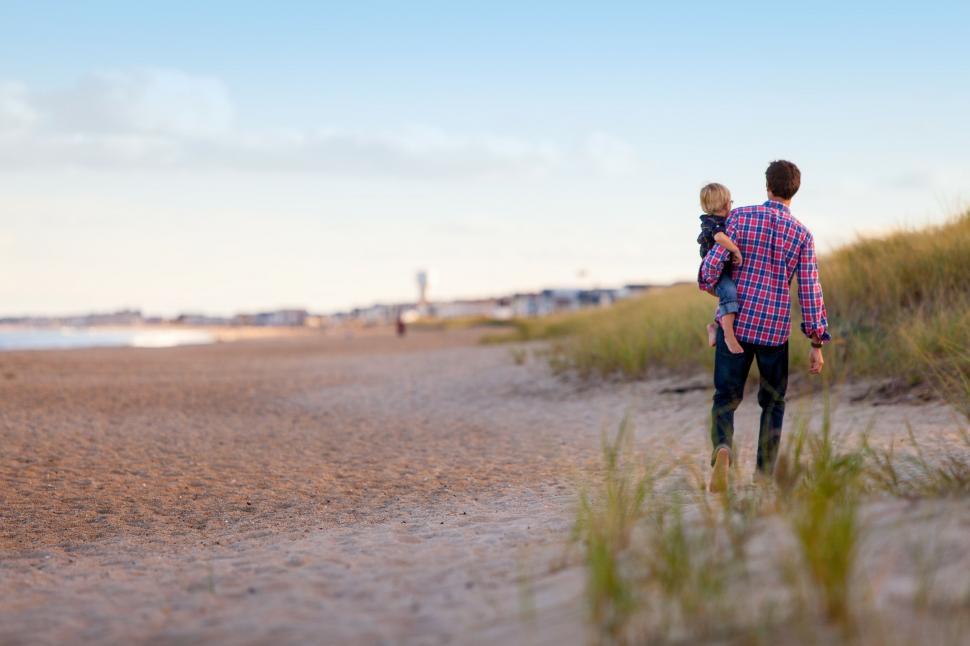 Free Image of Man Holding Baby Walking on Beach 