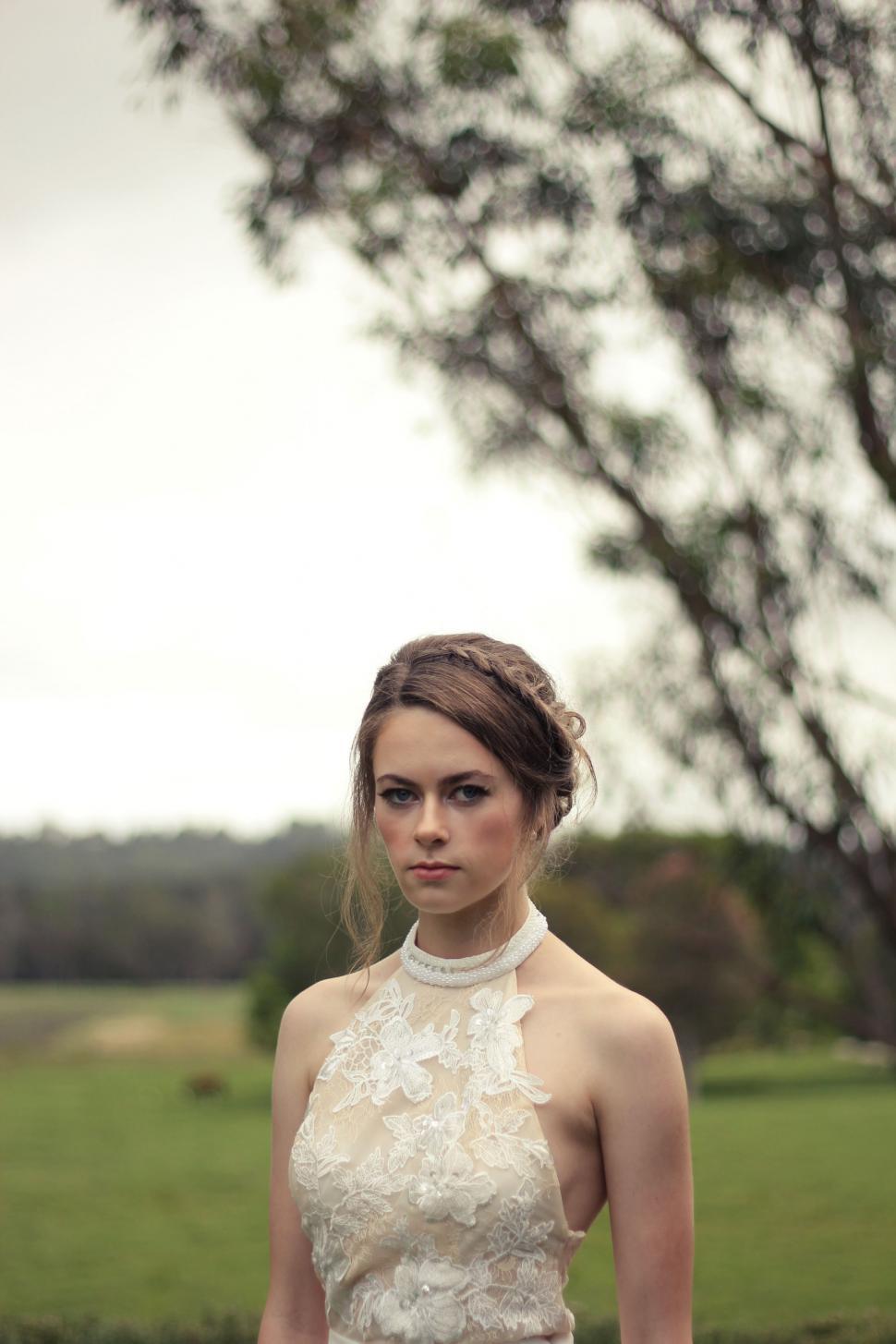 Free Image of Woman in White Dress Standing in Front of Tree 