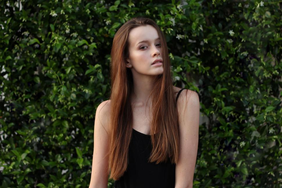 Free Image of Woman With Long Red Hair Standing in Front of Bush 