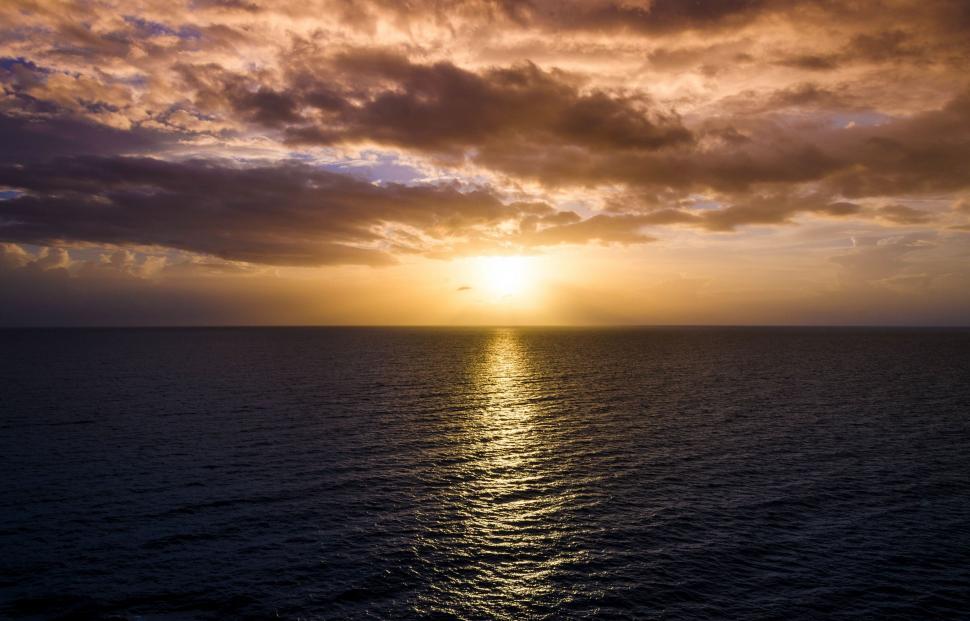 Free Image of Sun Setting Over Ocean on Cloudy Day 