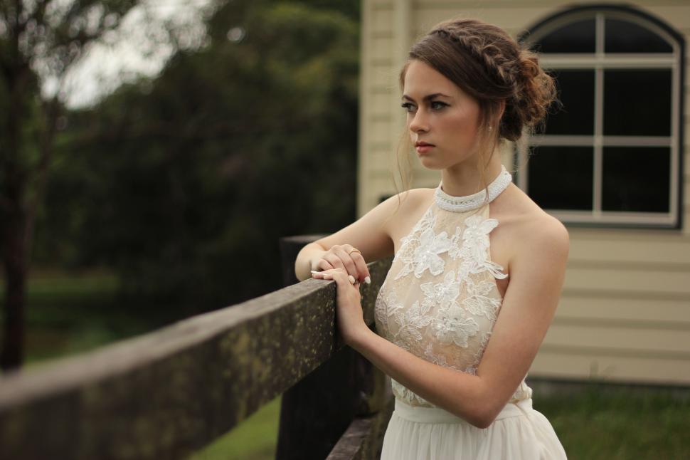 Free Image of Woman in White Dress Leaning on Fence 
