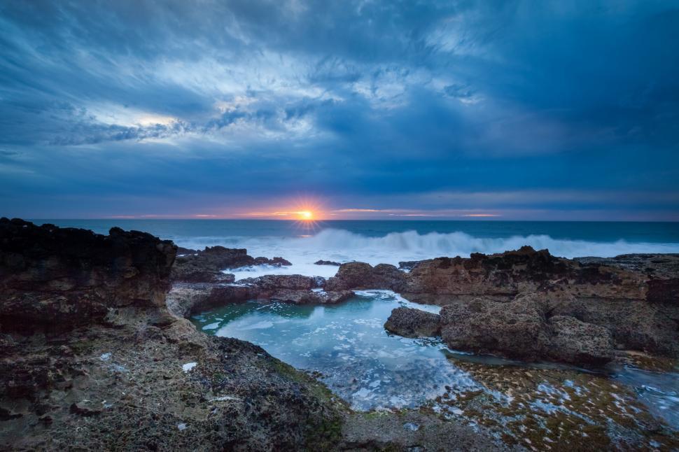 Free Image of Sun Setting Over Ocean on Cloudy Day 