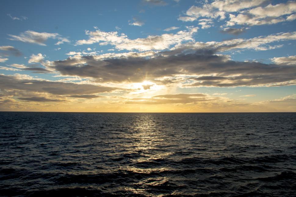 Free Image of Sun Setting Over Ocean on Cloudy Day 