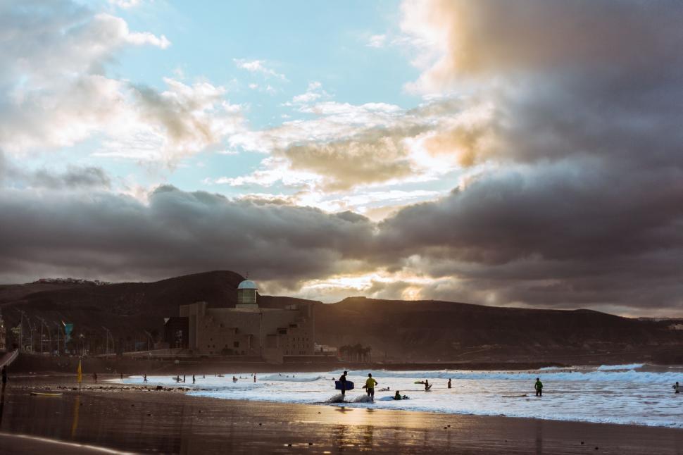 Free Image of Group of People Standing on Top of Beach Under Cloudy Sky 