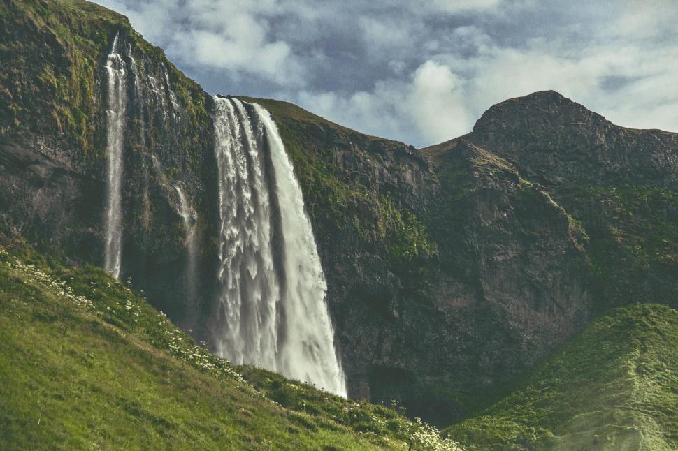 Free Image of Majestic Waterfall Cascading Down Lush Green Hillside 