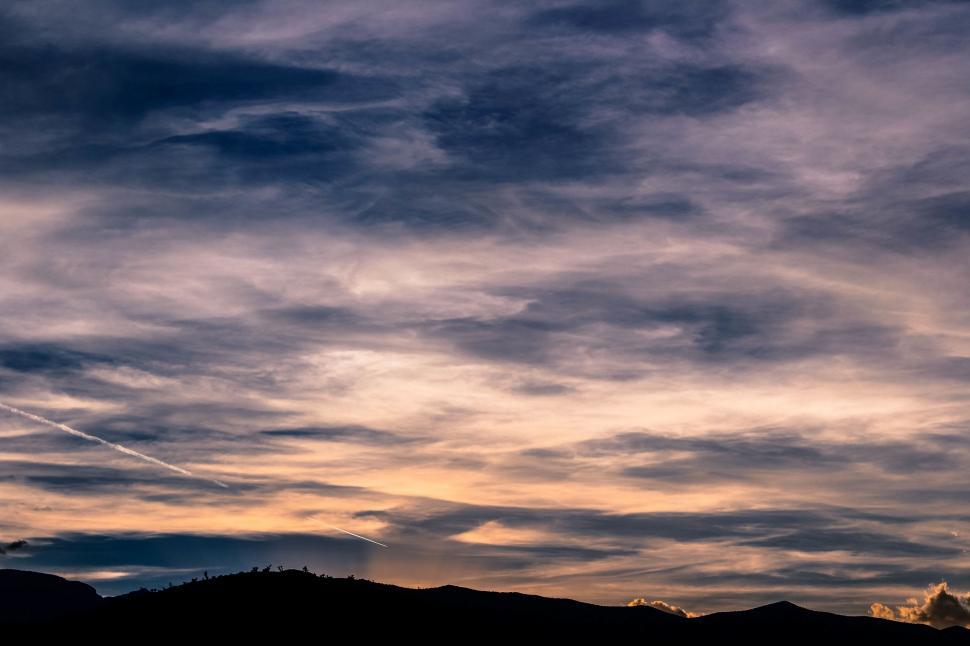 Free Image of Plane Flying Through Cloudy Sky With Mountains in Background 