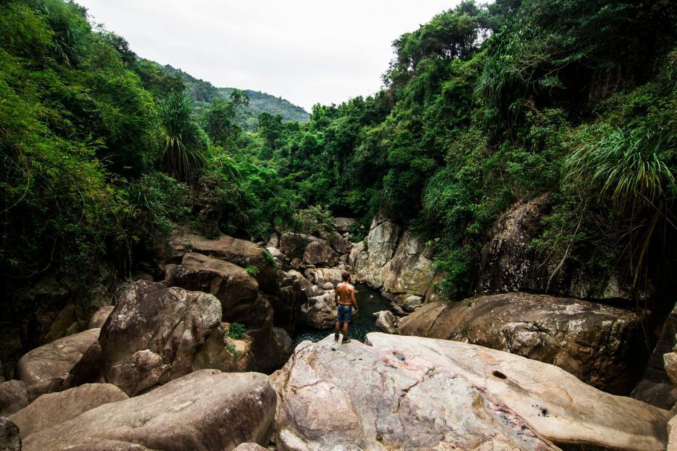 Free Image of Man Standing on Top of Large Rock Next to River 