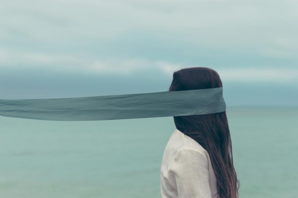 Free Image of Woman Standing on Beach With Long Ribbon Wrapped Around Her Head 