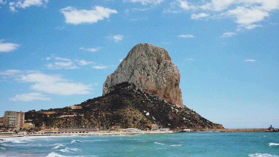 Free Image of Large Rock Jutting Out of Ocean by Beach 