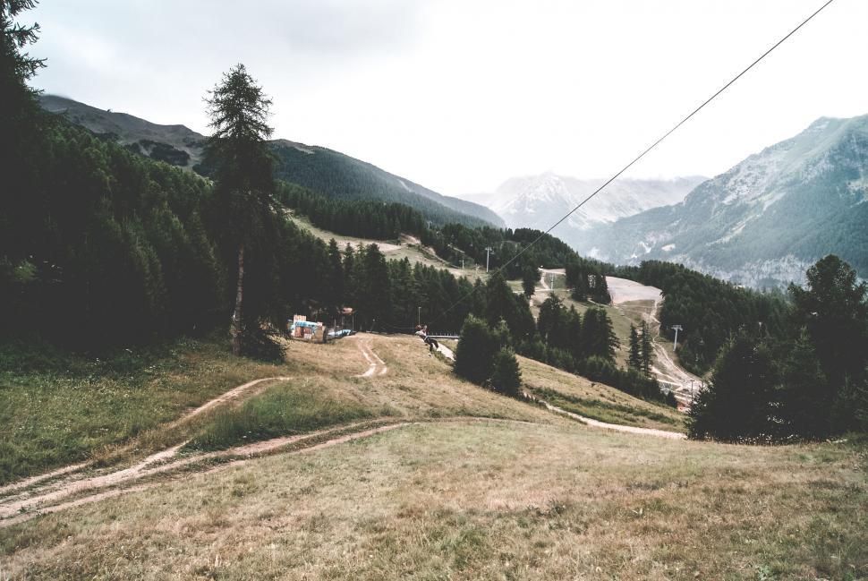 Free Image of Grassy Hill, Trees, and Mountains in Background 