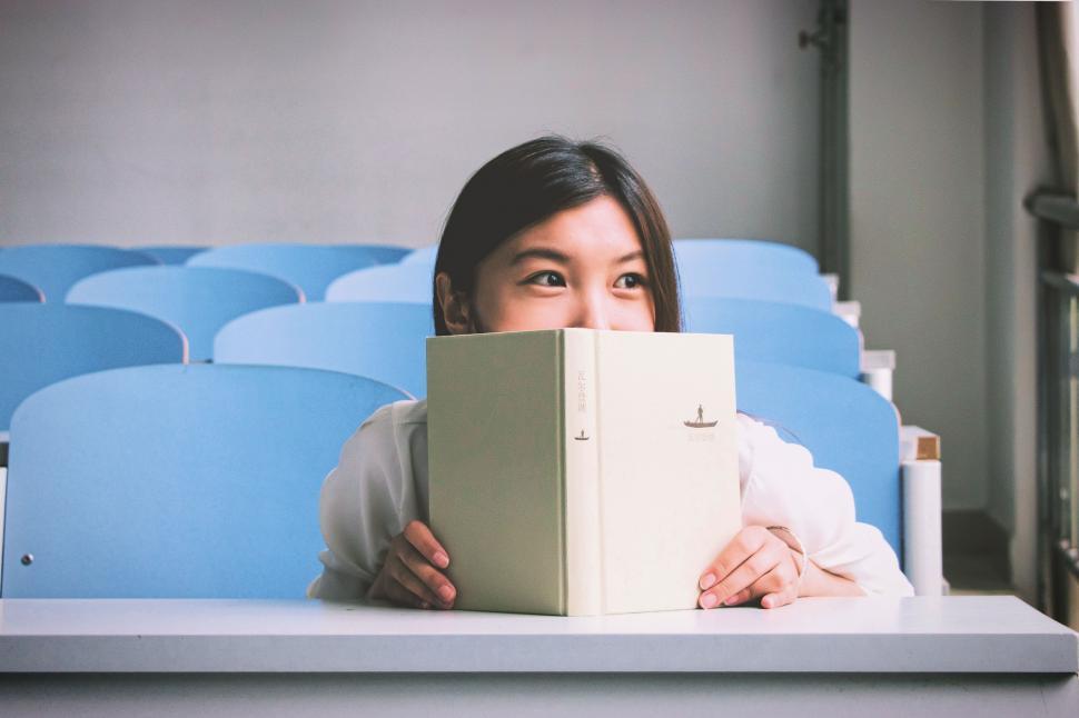 Free Image of Woman Hiding Face Behind Book 