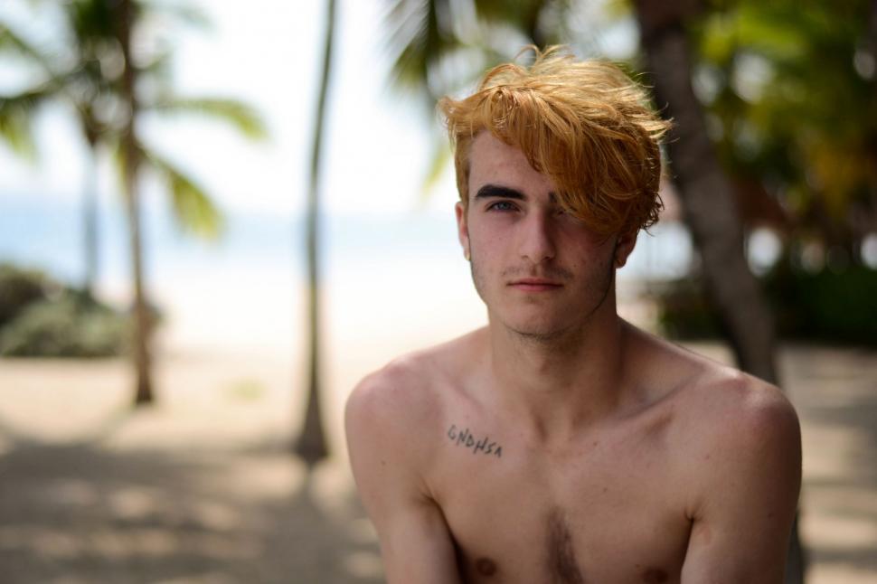 Free Image of Shirtless Man Standing on Beach Next to Palm Trees 