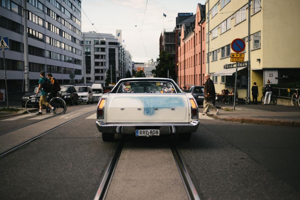 Free Image of White Car Driving Down Street Next to Tall Buildings 