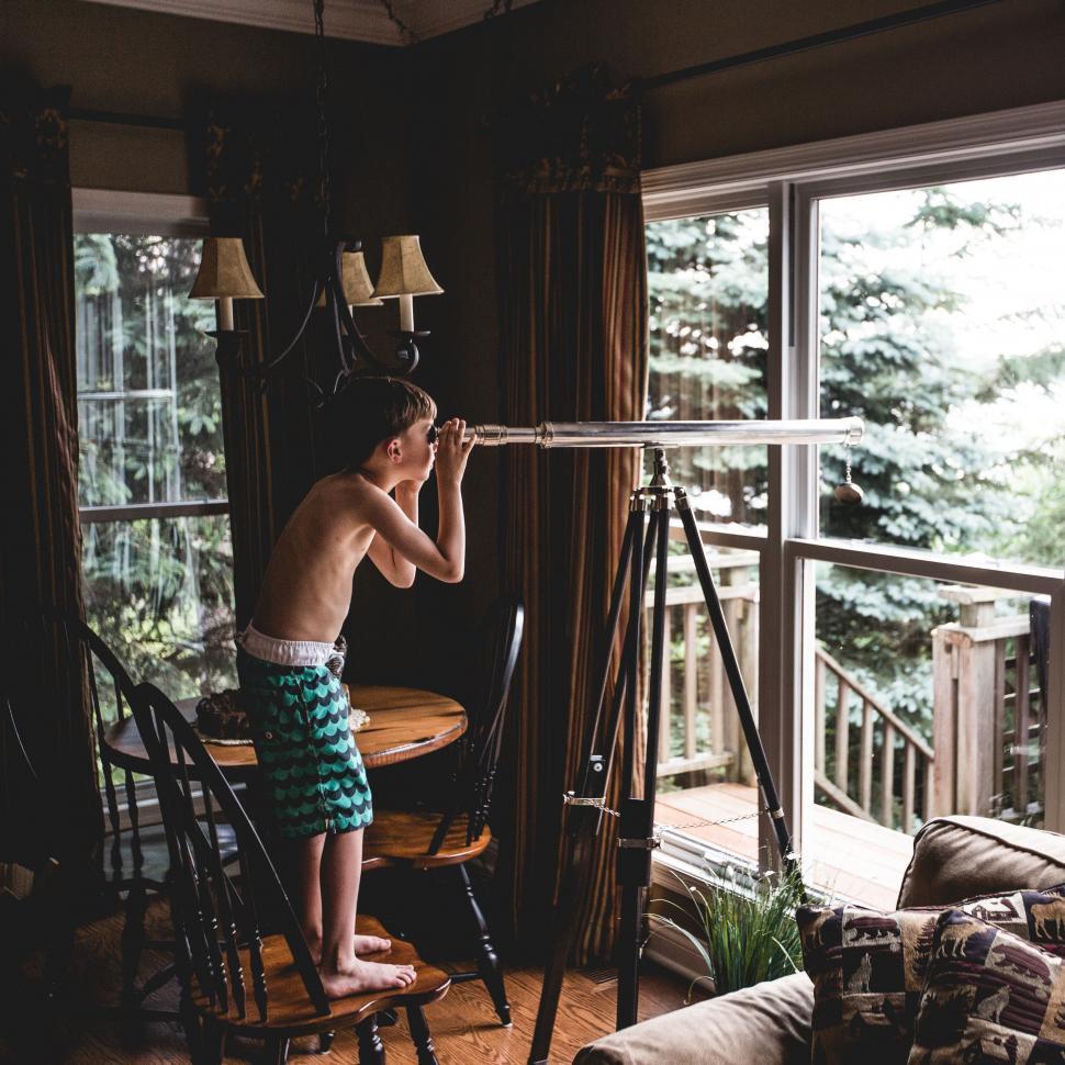 Free Image of Young Boy Standing on Chair Looking Through a Telescope 