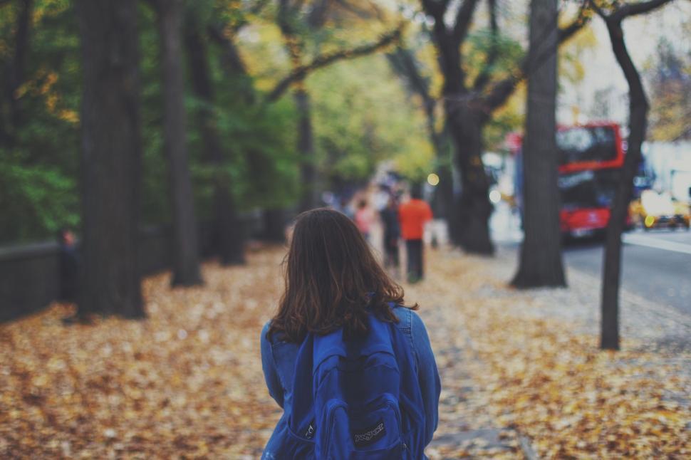 Free Image of Woman Walking Down Leaf-Covered Sidewalk 