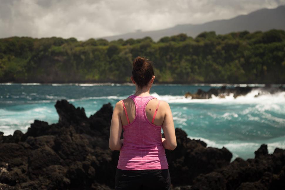 Free Image of Woman Standing on Rocky Beach Looking at Ocean 