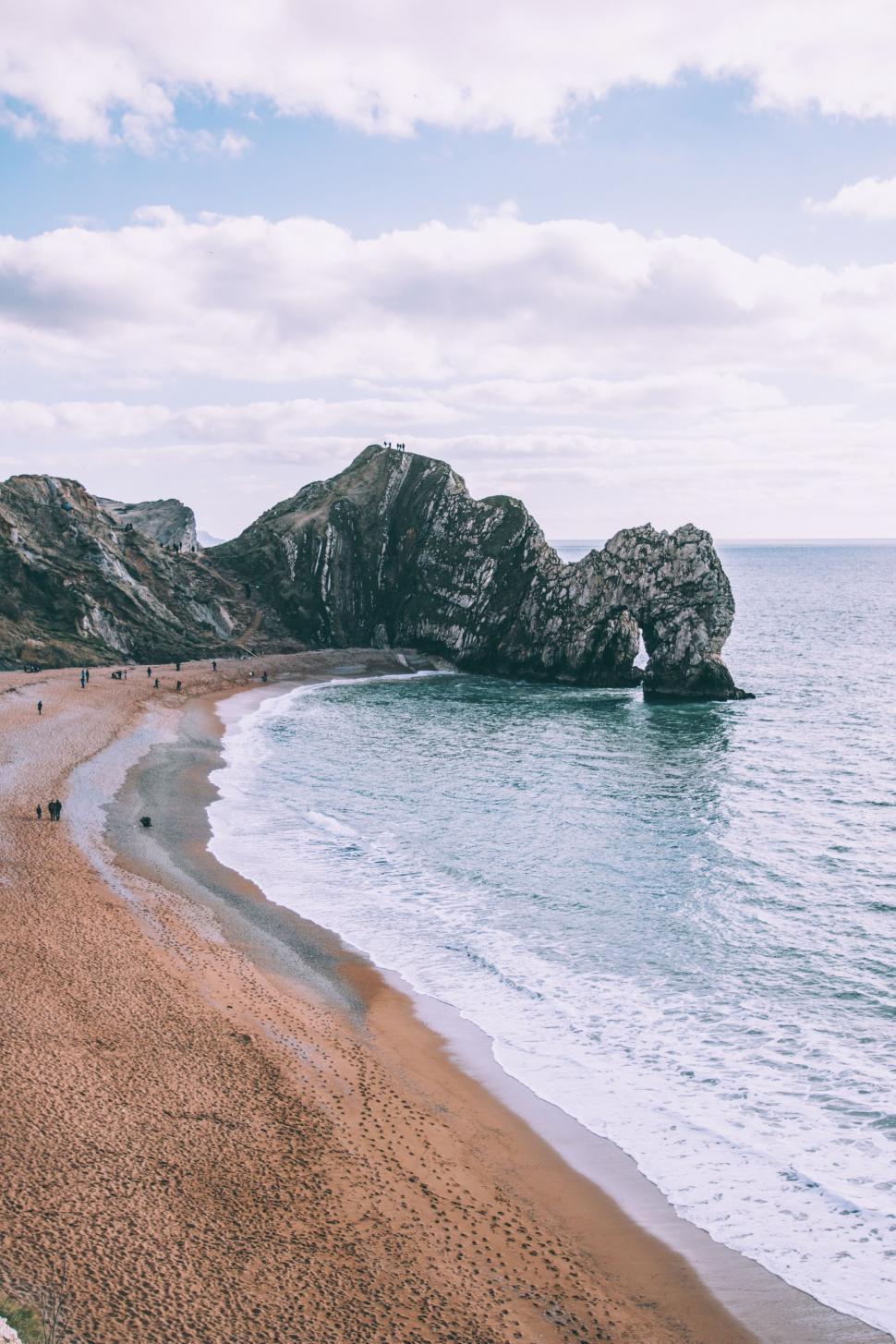 Free Image of Sandy Beach Alongside Ocean With Rocks in Background 