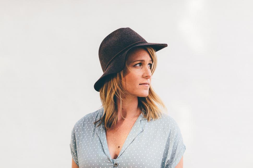 Free Image of Woman Wearing Hat Standing in Front of White Wall 