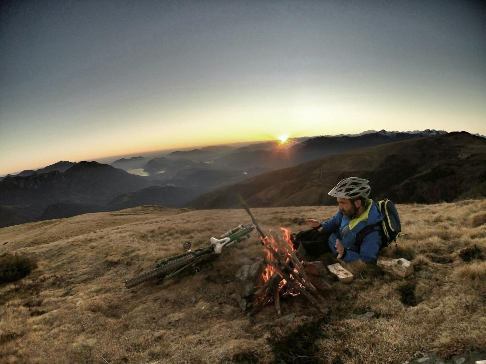 Free Image of Man Sitting by Fire on Grass-Covered Hillside 