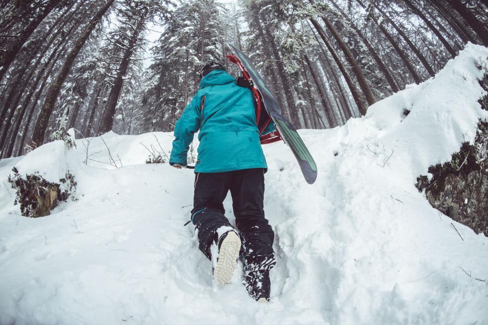Free Image of Person Walking Up Snowy Hill With Snowboard 