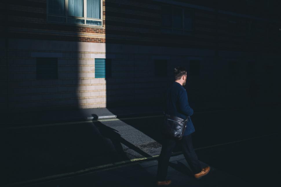 Free Image of Woman Walking Down Street Next to Tall Building 